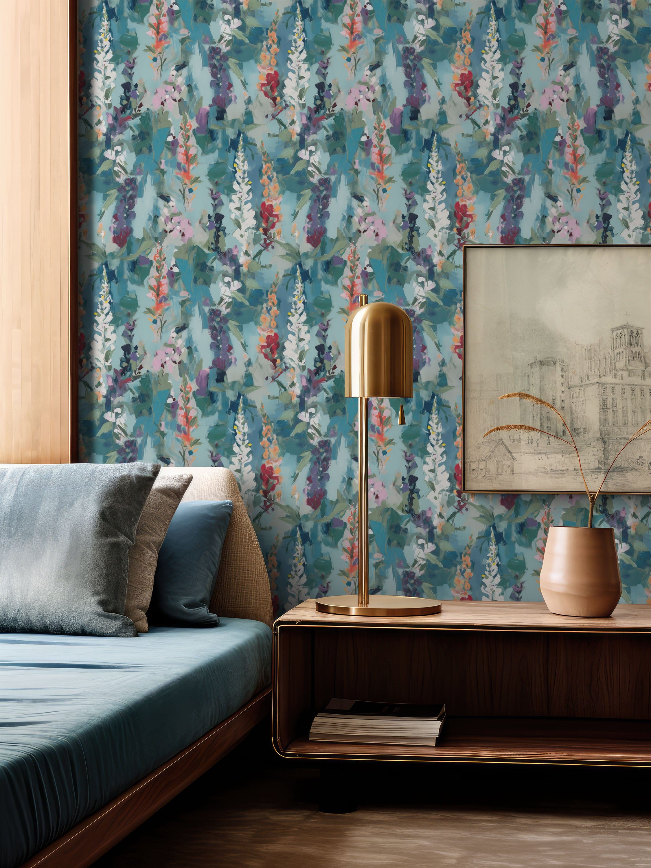 Painterly floral wallpaper in teal and soft blue tones, styled in a modern bedroom with a brass table lamp, wooden bedside unit, and framed artwork.