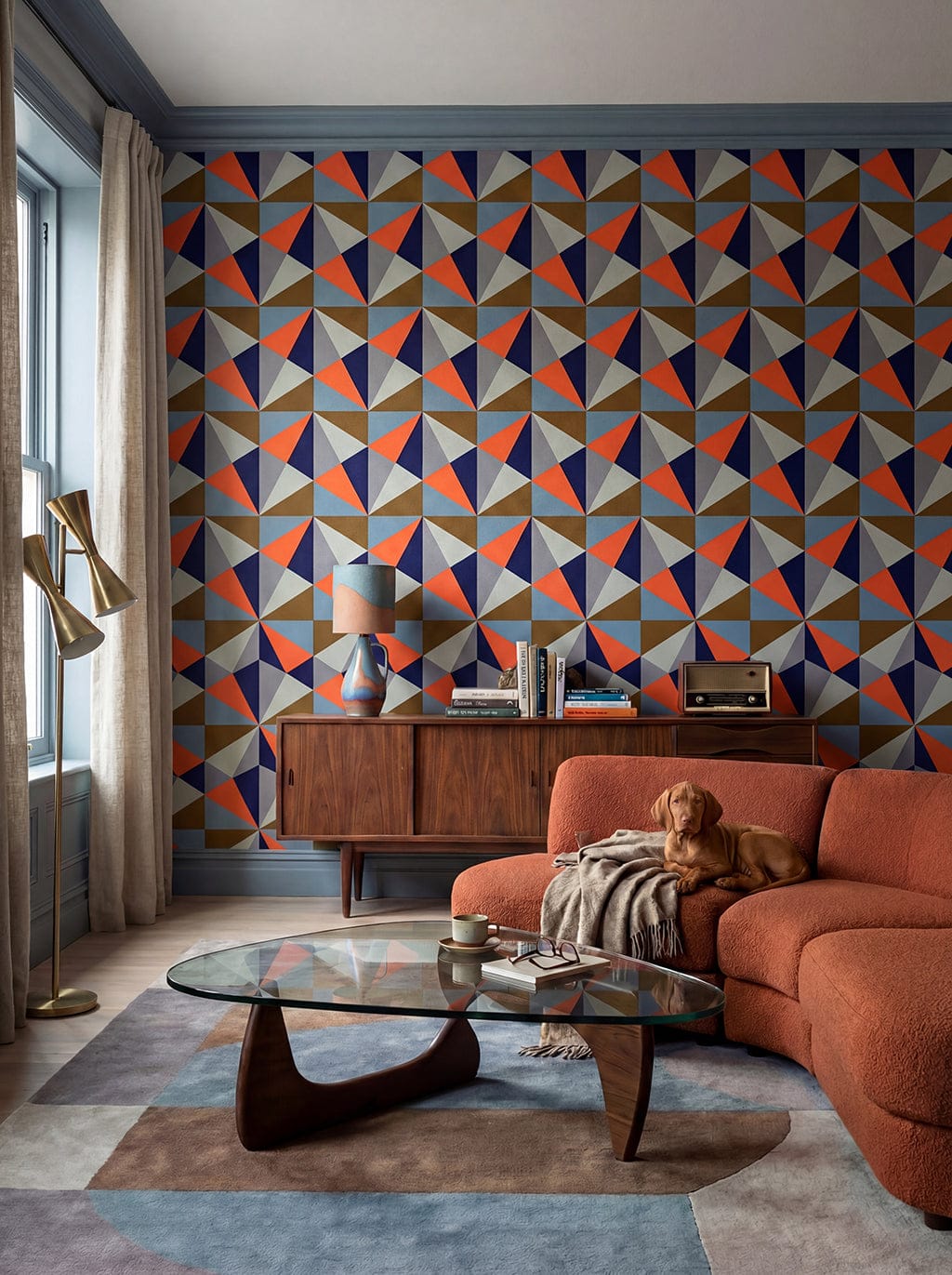 Modern living room with geometric wall pattern, orange sofa, and glass coffee table.