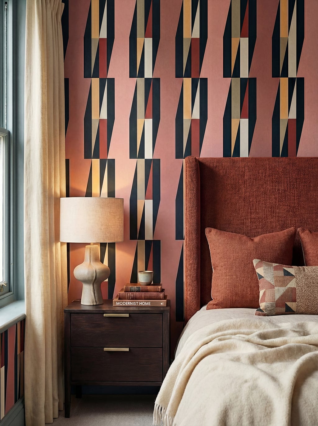 Modern bedroom with geometric patterned wallpaper, bed with pillows, and nightstand with lamp.