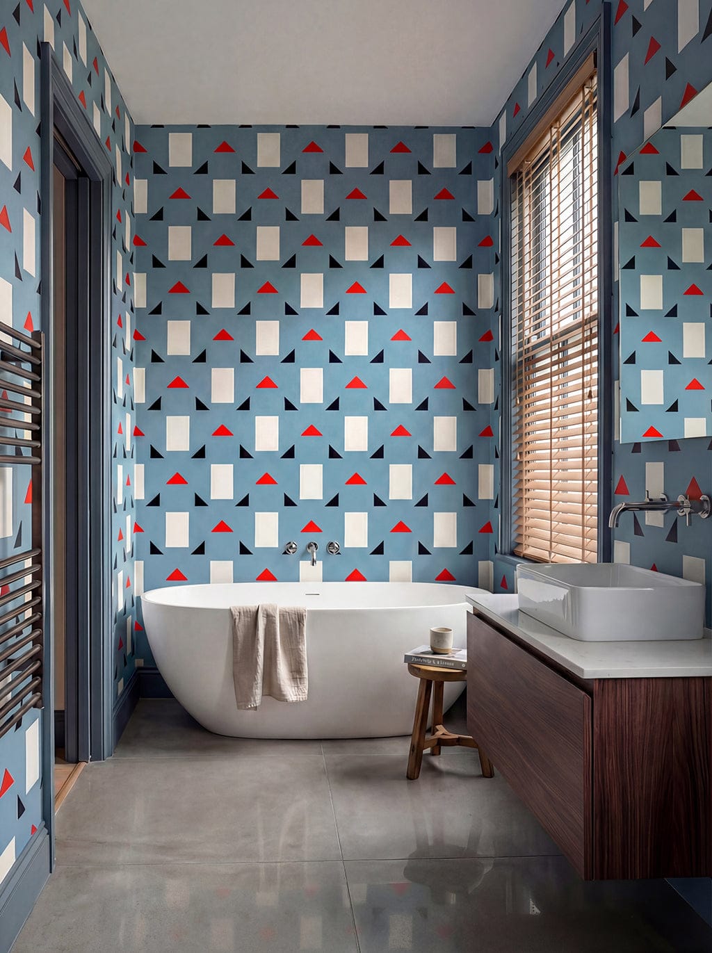 Modern bathroom with geometric patterned wallpaper, freestanding bathtub, and wooden vanity.