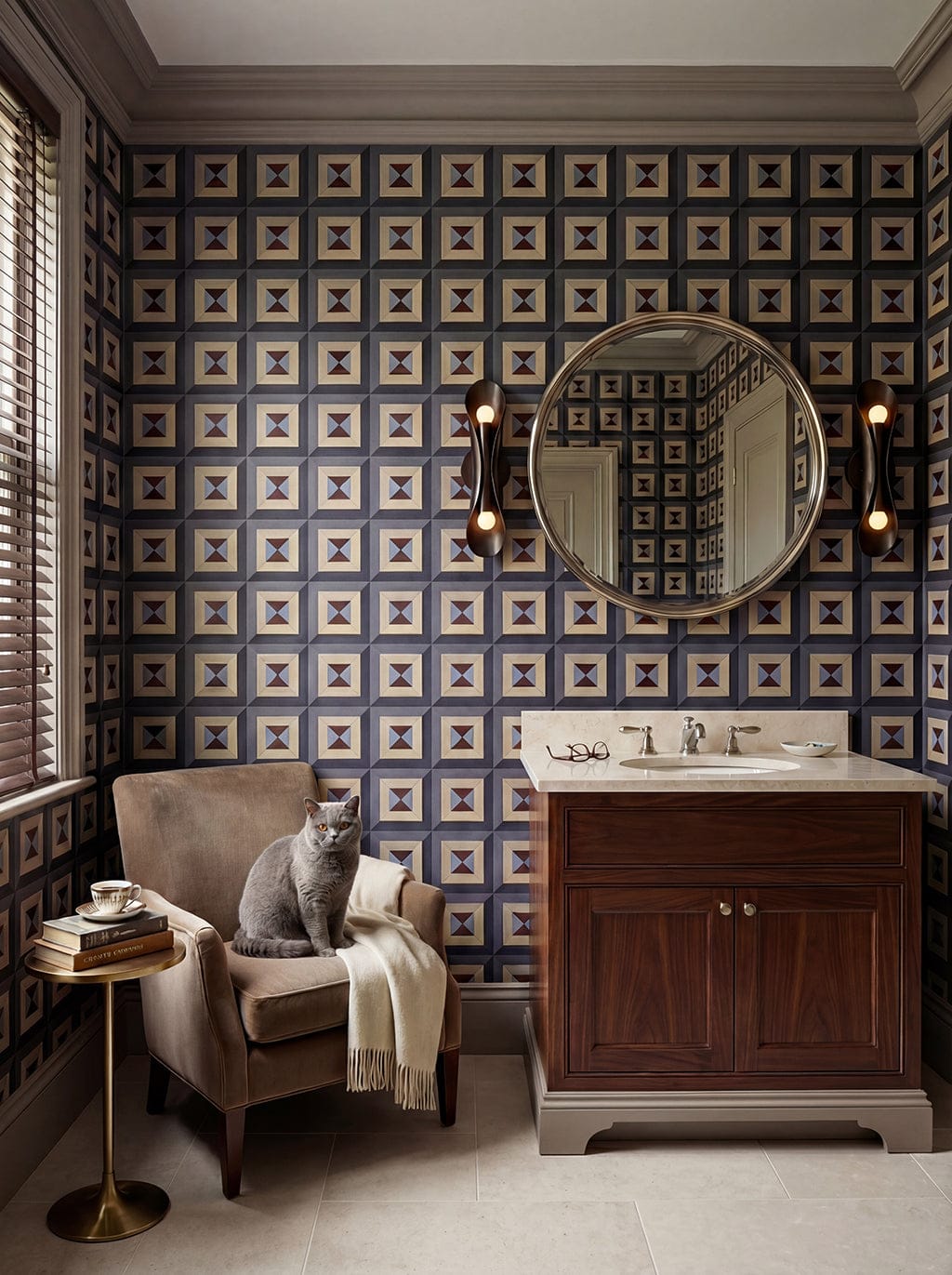 Bathroom with patterned wallpaper, wooden vanity, and armchair with a cat.