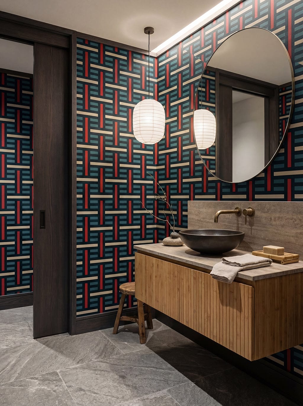Bathroom with geometric patterned wallpaper, wooden vanity, and round mirror.